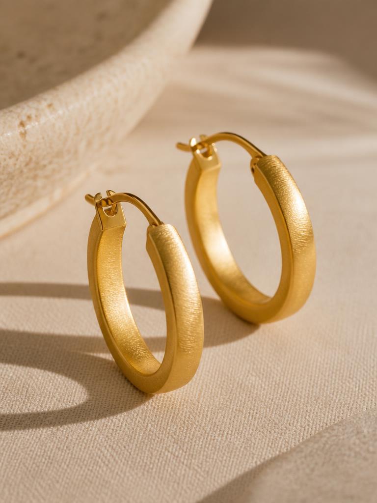Pair of brushed gold hoop earrings resting on soft linen