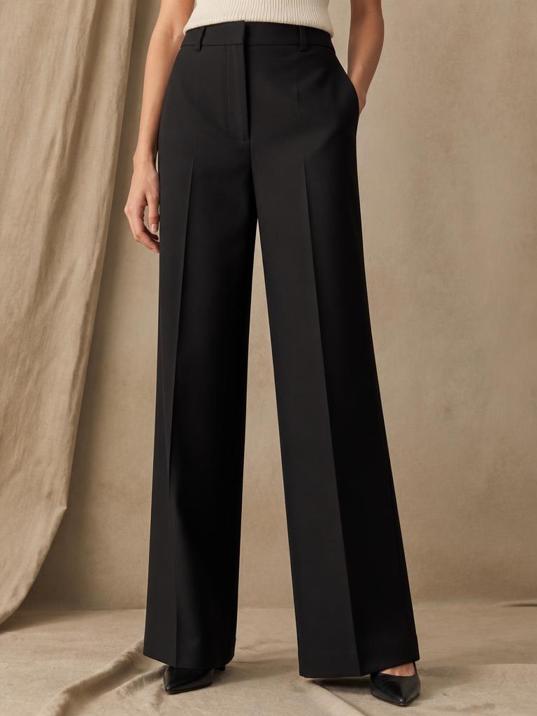 Model wearing black wide leg tailored trousers with a pressed centre crease